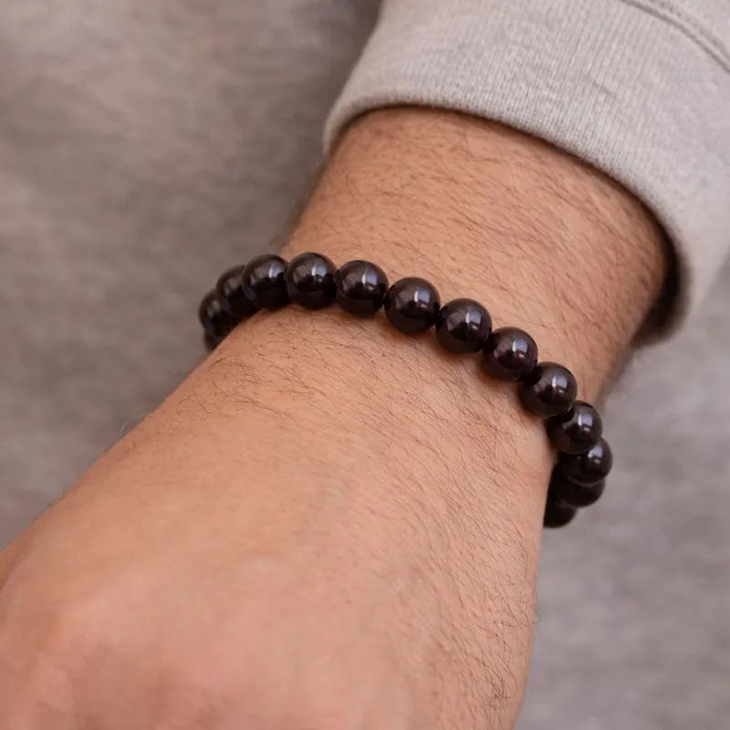 Bracelet en grenat naturel porté au poignet d’homme, perles rondes rouges bordeaux.