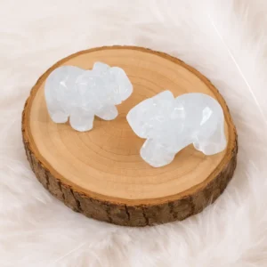 Éléphant en cristal de roche naturel posé sur rondin en bois, fond plumes blanches