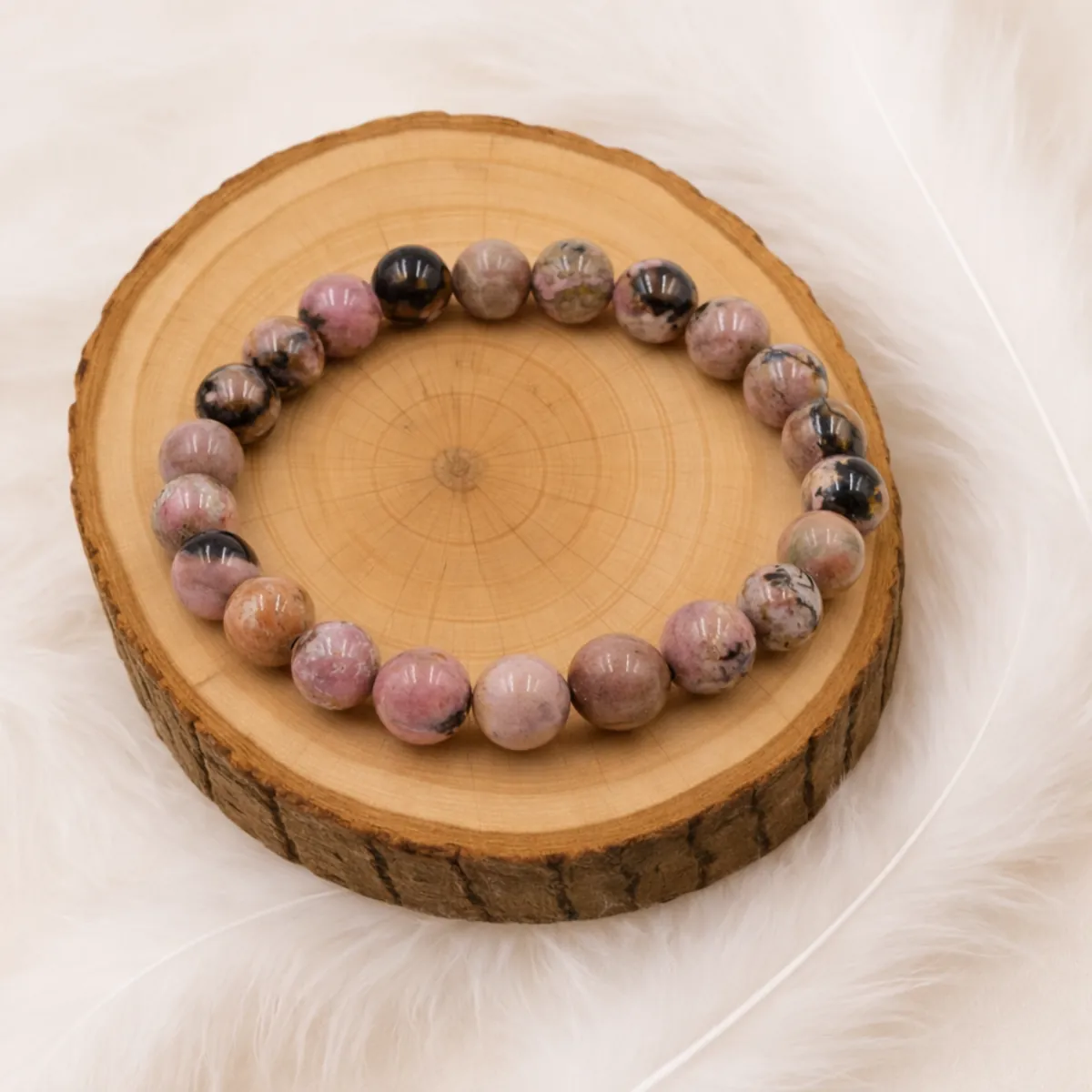 Bracelet rhodonite en pierre naturelle posé sur un rondin de bois