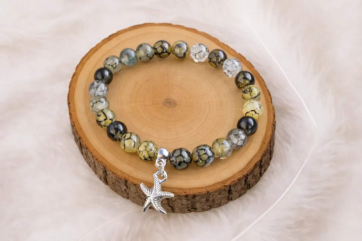 Bracelet en agate veine de dragon avec breloque étoile de mer posé sur rondin de bois