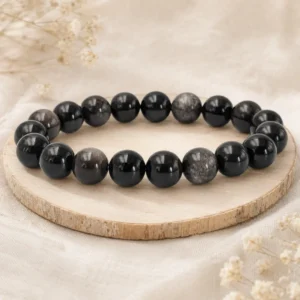Bracelet en obsidienne argentée posé sur un rondin de bois clair