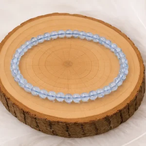 Bracelet en topaze bleue naturelle, perles 6 mm, présenté sur un rondin en bois.