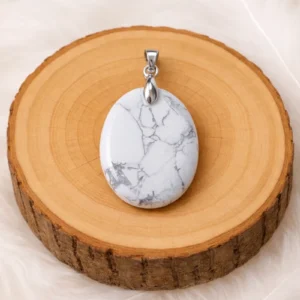 Pendentif ovale en howlite blanche veinée grise posé sur un rondin de bois.