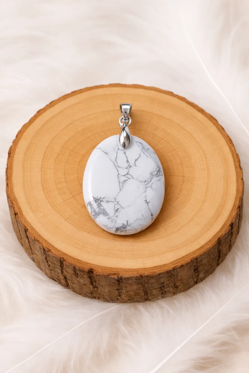 Pendentif ovale en howlite blanche veinée grise posé sur un rondin de bois.
