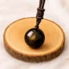 Pendentif sphère en obsidienne dorée posé sur rondin en bois