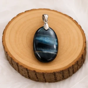Pendentif Œil de Faucon oval posé sur un rondin en bois, pierre naturelle aux reflets bleutés protecteurs