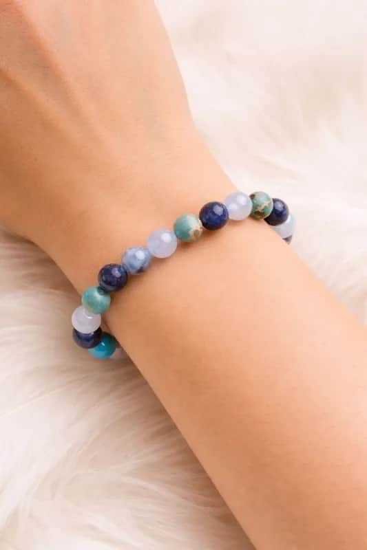 Bracelet en pierres naturelles bleu et turquoise porté au poignet, sur fond blanc duveteux.
