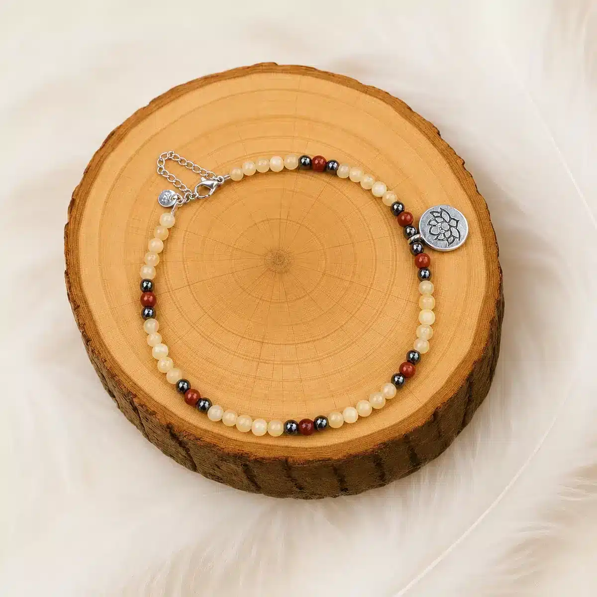 Bracelet de cheville calcite hématite jaspe rouge présenté sur un rondin de bois