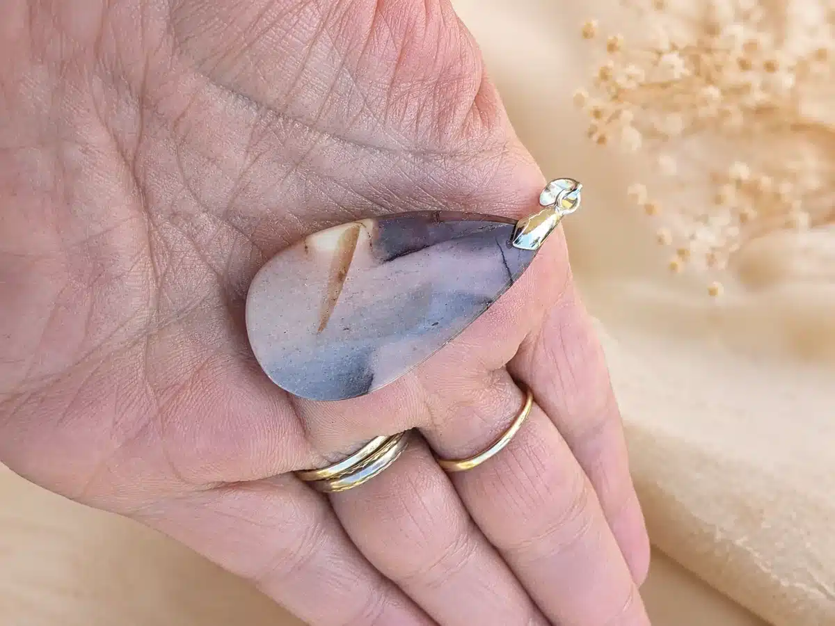 Dos Pendentif en Jaspe Mokaïte naturel aux nuances roses, grises et beiges tenu dans une main
